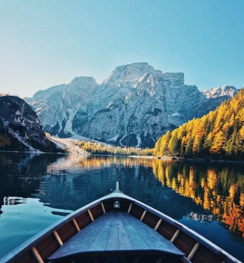 Experience a tranquil boat journey in Lago di Braies, Italy with stunning mountain views.