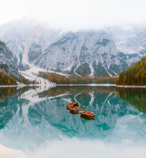 Tranquil mountain lake with wooden boats and stunning reflections amidst autumn foliage.
